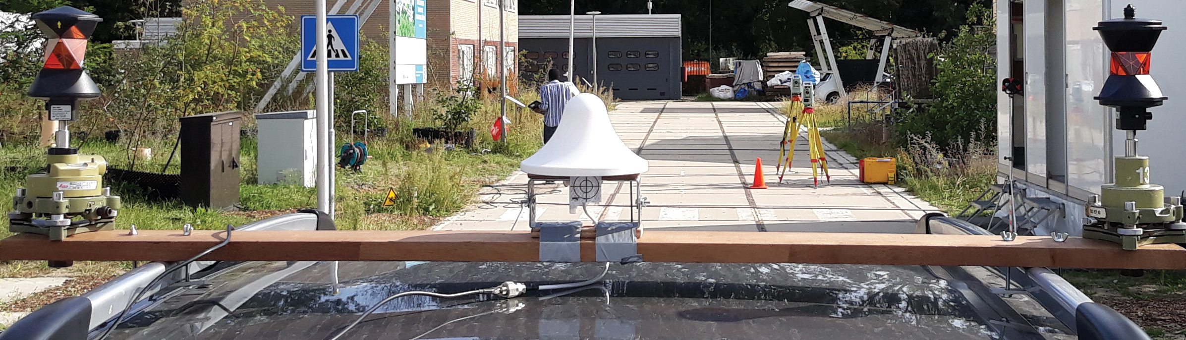 FIGURE 5 Receiver antenna mounted on the roof of a car. Two 360° prisms are used to determine the receiver ground-truth positions at the millimeter level, by means of land surveying total stations (placed on the yellow tripods in the distance).
